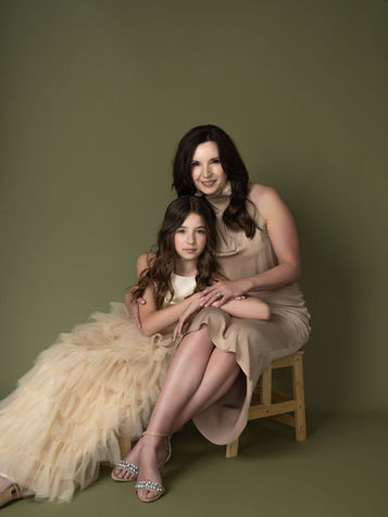 Mother and daughter sitting closely on a wooden stool, both wearing soft neutral dresses, captured in a legacy portrait session in Durham