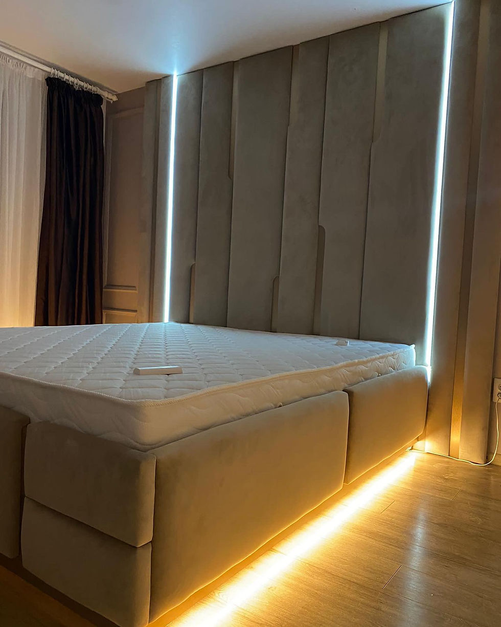 Miniatură: Dormitor modern si luminos cu pat tapitat cu tablie inalta si insertii metalice aurii si benzi de iluminat cu LED.