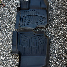 Two black WeatherTech floor mats on a stone surface for vehicles