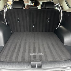 Clean car trunk with carpet and a person in the reflection, ready to go.