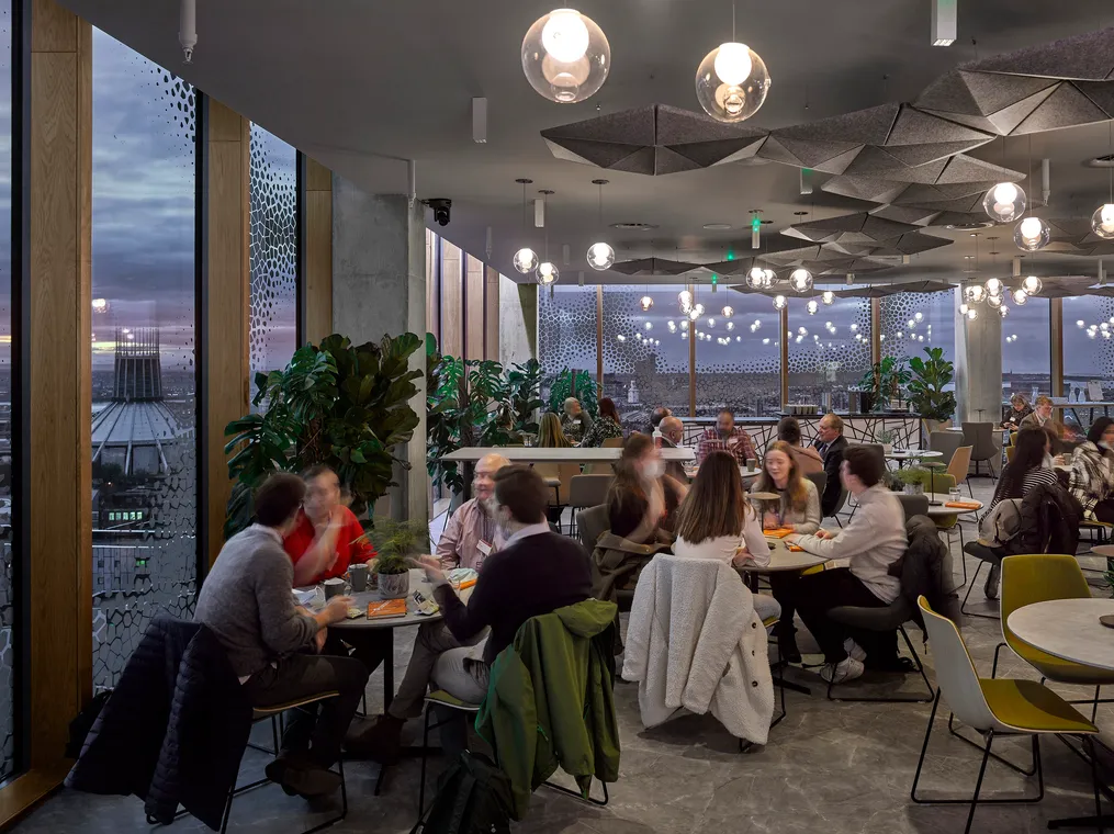 mensa con tavoli tondi, luci sferiche, piante e pannelli geometrici sul soffitto