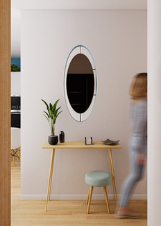 Ingresso con specchio ovale a parete, consolle in legno chiaro con sgabello turchese e pianta in vaso, divisorio in legno sulla sinistra e persona in movimento sullo sfondo.