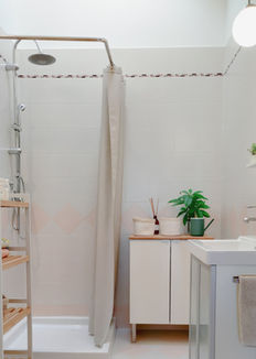 Bagno compatto con doccia a tendina, mobile lavabo bianco, scaffale in legno e numerose piante decorative.