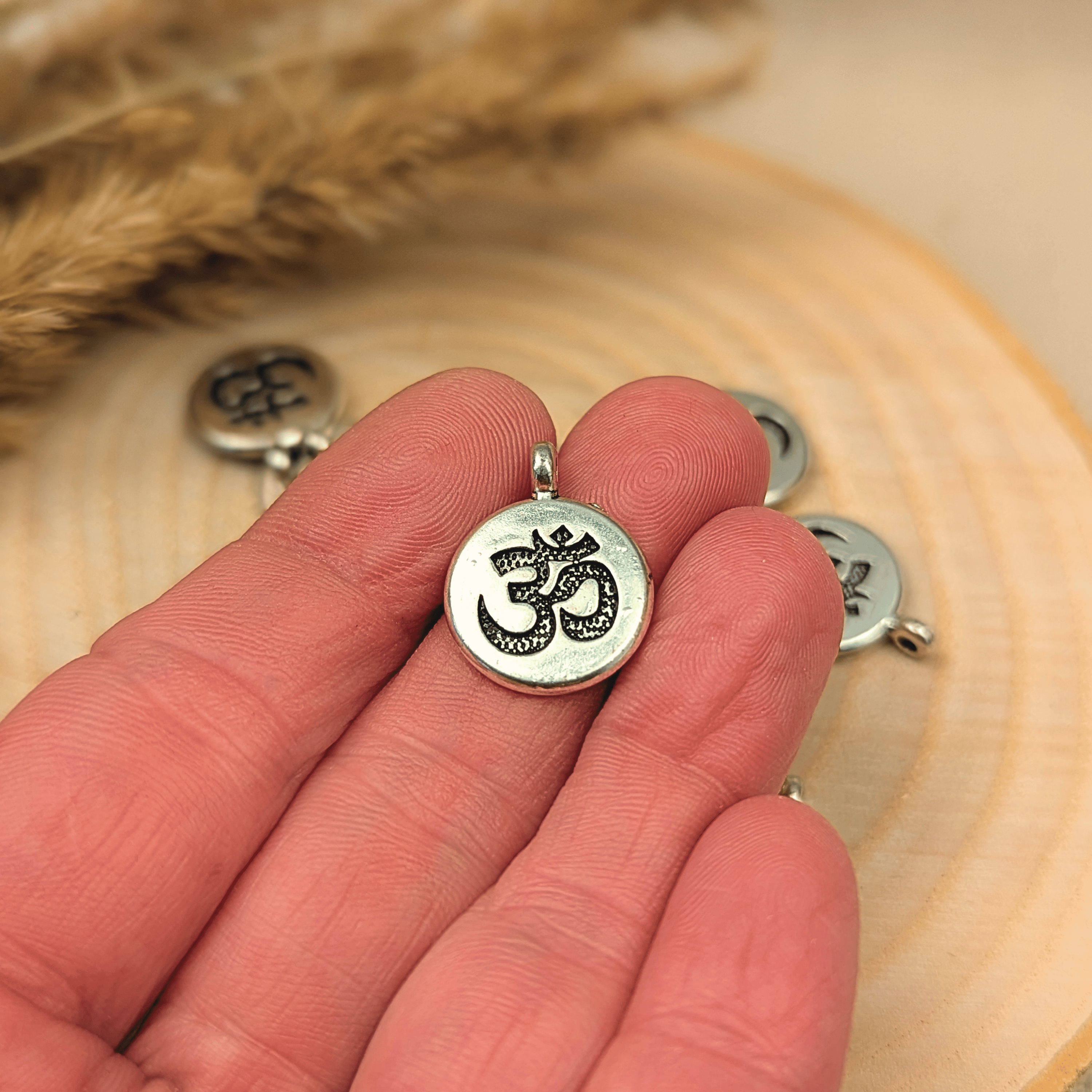Fünf silberne Ohm-Anhänger aus Metall auf einer Holzscheibe. Spirituelles Zubehör zum Schmuck selber machen für Yoga-Armbände