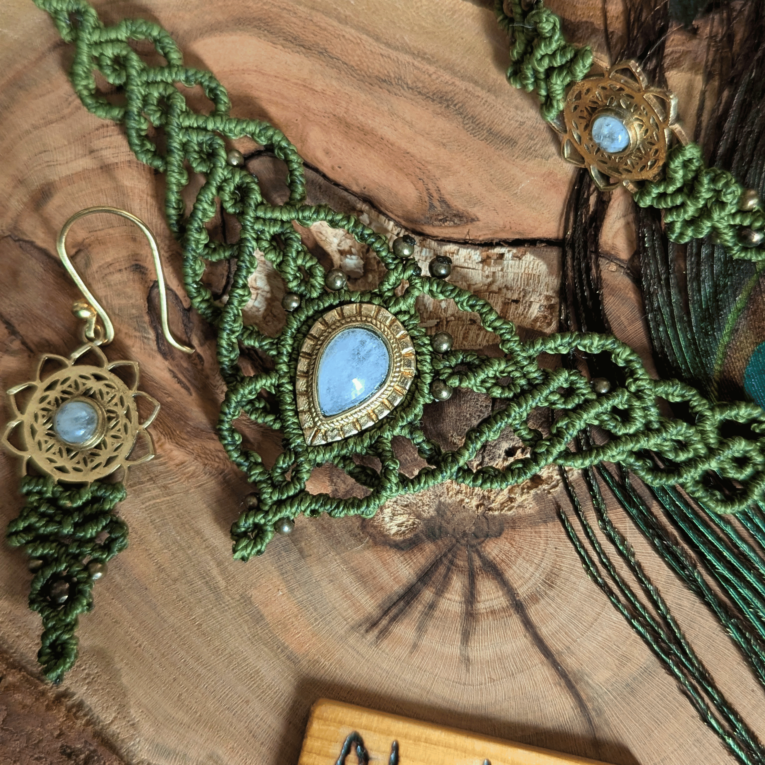 Detailansicht der Makramee-Kette „Elfenlight“ in Olivgrün mit eingefasstem Mondstein-Edelstein auf einer Pfauenfeder und Holz