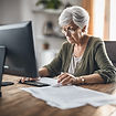 older woman sitting in front of computer reviewing paper documents.jpg
