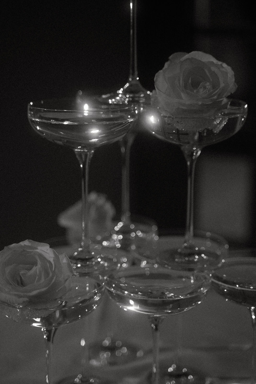 Stacked champagne coupe glasses with a white rose detail, styled for an elegant wedding reception in a moody setting