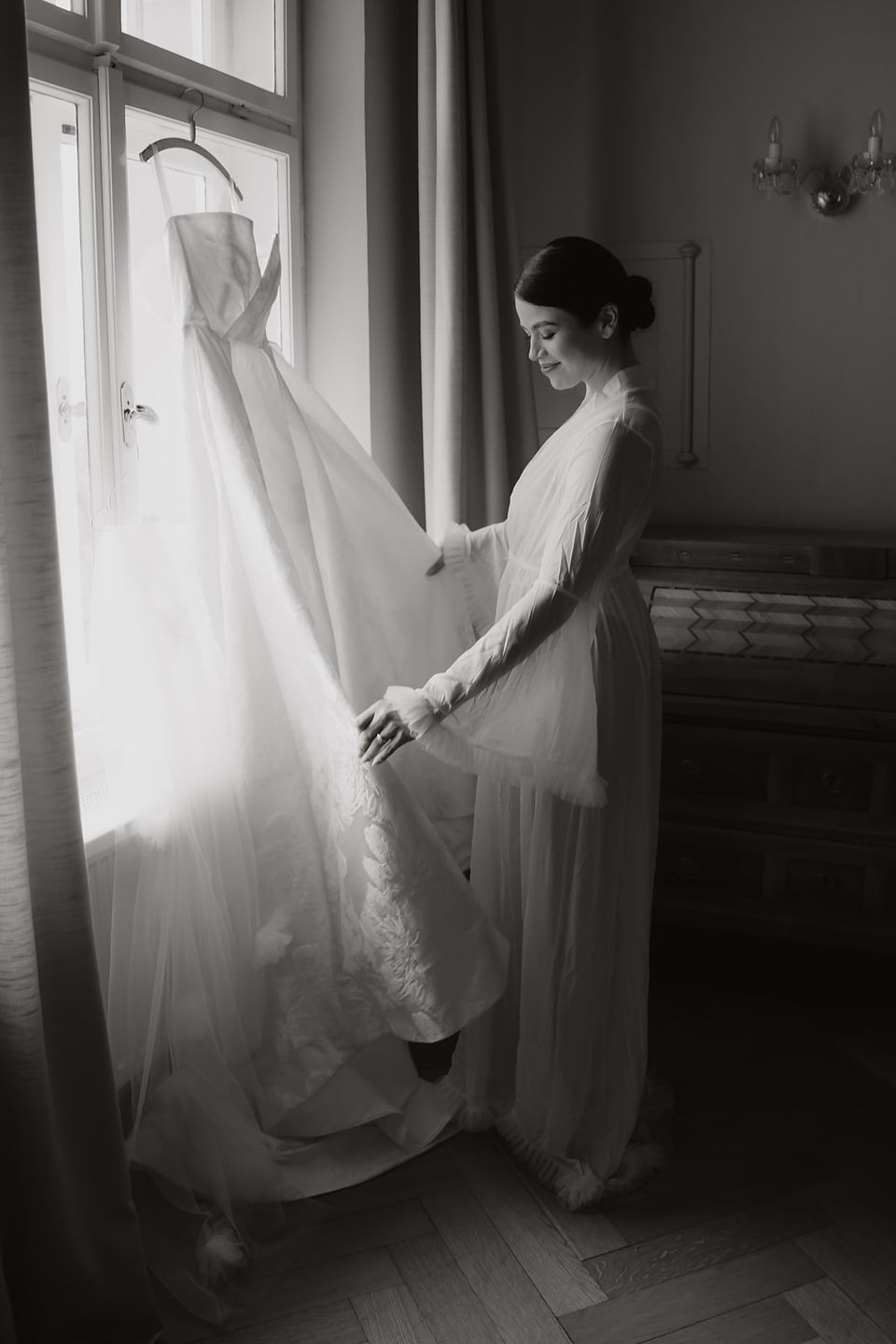 Bride standing by the window with her wedding dress during a quiet moment before the ceremony