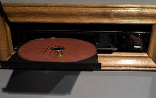 A picture of a framed pass-through slot in a wall. The slot is occupied by a Blu-ray player with its disc drawer open.