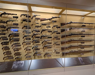 A museum display case containing various Civil War-era handguns, rifles, and carbines, including Colt and Springfield models.