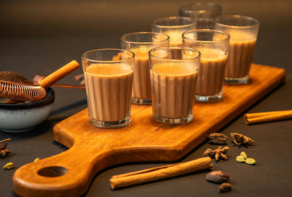 A wooden tray adorned with glasses of creamy milk tea, surrounded by aromatic spices like cinnamon and cardamom.