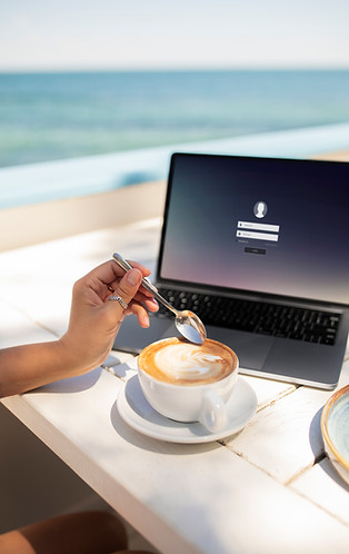 Side view of a hand holding a spoon while workingon a laptop, representing multitasking during remote work