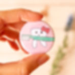Hand holding a pink button pin of a tooth carrying a toothbrush