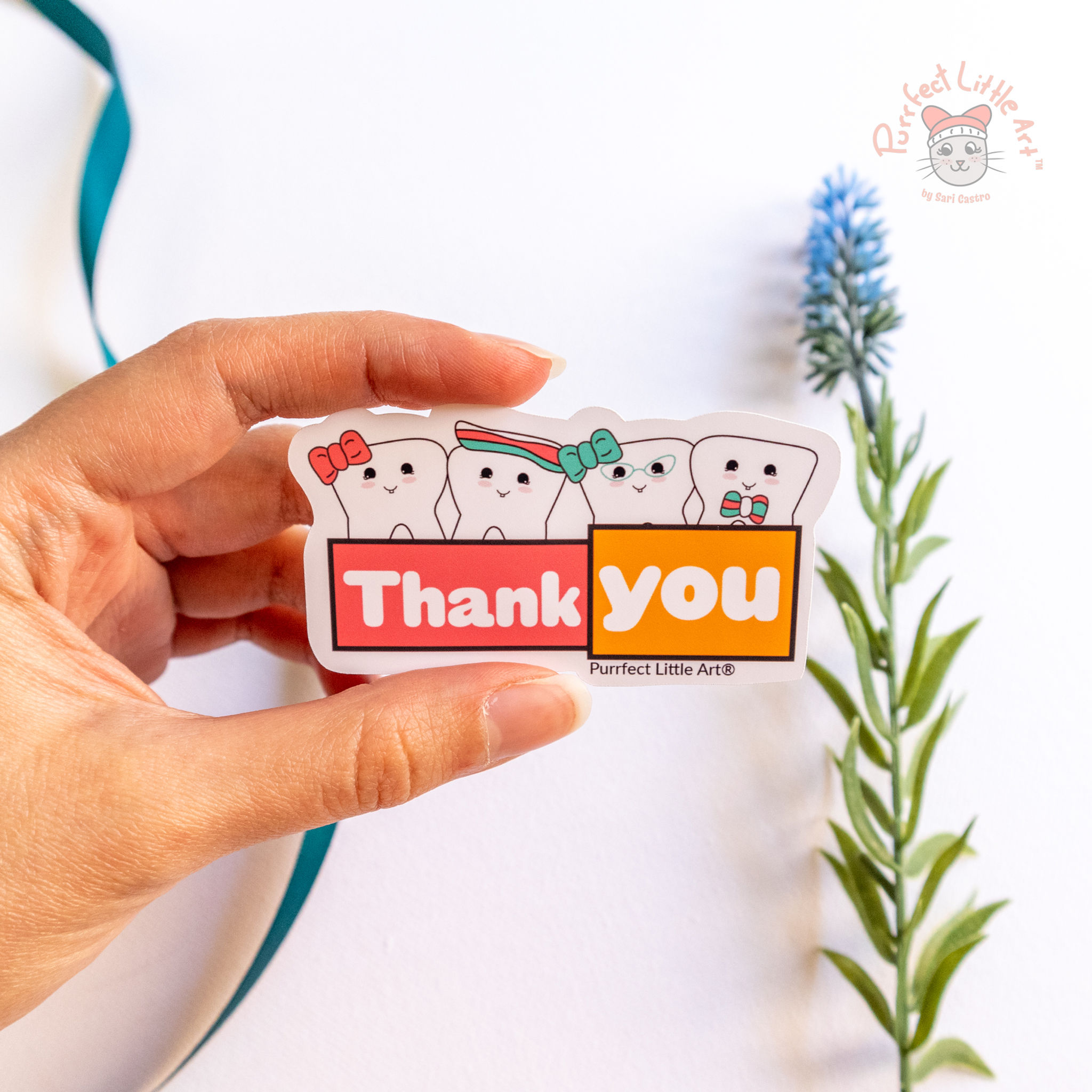 Hand holding a whimsical dental themed sticker with tooth characters holding a banner that says "thank you"