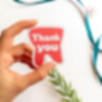 Hand holding a pink tooth-shaped sticker that reads "thank you"