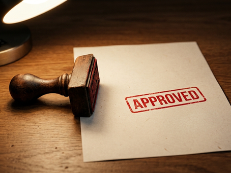 A wooden desk stamp lying on its side beside a sheet of paper marked APPROVED in red ink