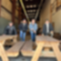 Workers pose on picnic tables in a warehouse. The workers are dressed in winter attire.