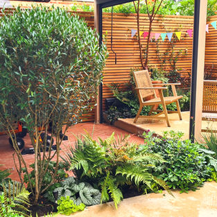 Compact Chiswick townhouse garden with a low pergola, wooden seating, Dutch pavers and soft evergreen planting creating a calm, modern retreat.