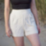 Natural linen-blend high-waisted shorts with pleated front, styled with black strappy crop top
