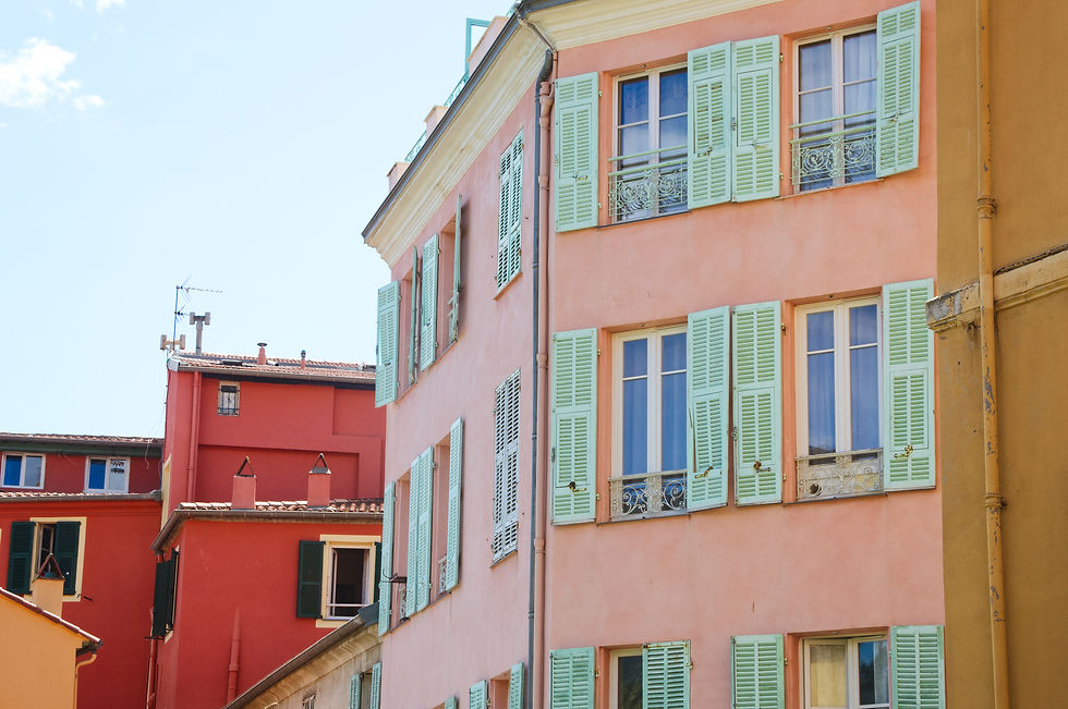 Colorful buildings in Menton, France, with pastel shutters under a clear blue sky, conveying a bright, cheerful Riviera street scene.