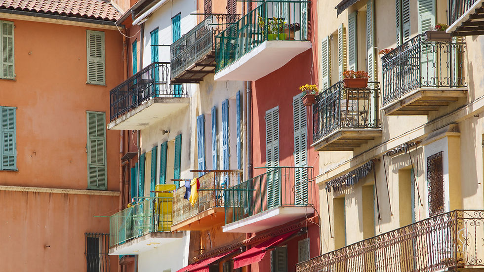 Colorful urban building with bright shutters and balconies, decorated with plants and laundry. Sunny, cheerful Mediterranean vibe.