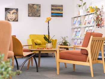 Coin salon chaleureux aménagé dans une médiathèque : fauteuils confortables aux tons terracotta et jaune moutarde, table basse en bois, plantes et espace lecture convivial créant une ambiance douce et accueillante, pensée comme un véritable lieu de détente et d’échange.