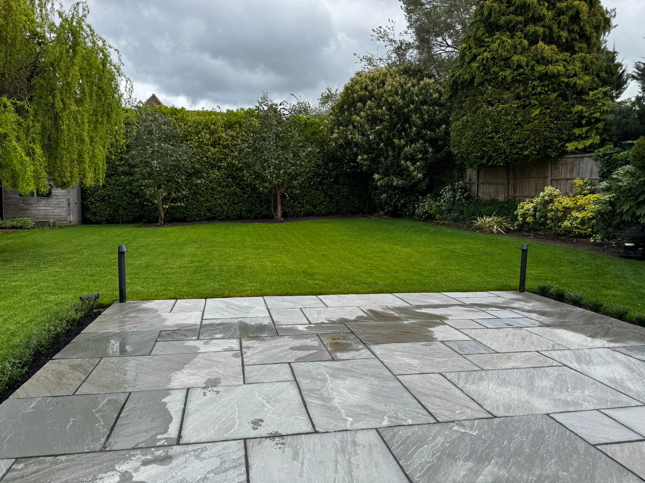Garden lawn bordered by planting and a stone patio
