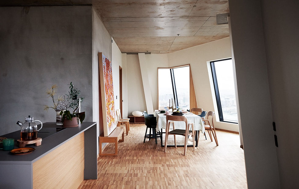 Interior of a Vertikal Nydalen apartment featuring exposed concrete ceilings, oak window sills, and minimalist furnishings. The space reflects a natural, elemental aesthetic with abundant daylight and a warm oak parquet floor.