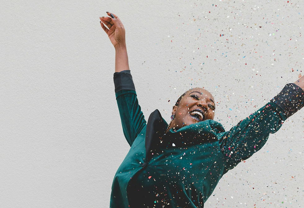 A joyful woman, engulfed in a shower of colorful confetti, beams with happiness against a simple white background.