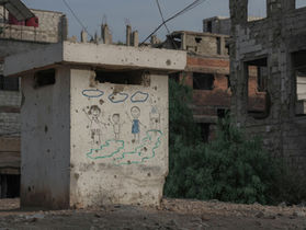     A child's colorful drawing of a smiling family and house stands out against the backdrop of damaged buildings.
