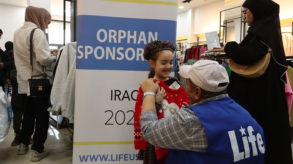 Photo of a LIFE team member outfitting a young girl with new clothes and making her smile.