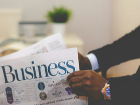 A man in a suit reads the business section of a newspaper, focusing on market trends and economic news.