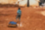 Photo of a boy dragging a wagon through the mud in a displacement camp. 