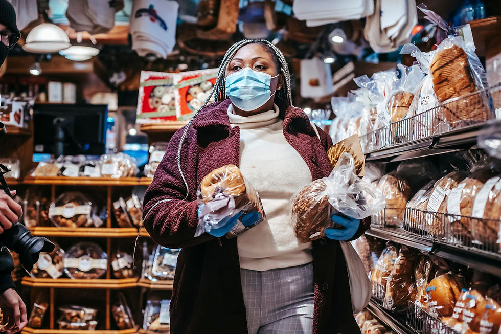 A woman, wearing a face mask and gloves, carefully selects freshly packaged bread from the shelves.