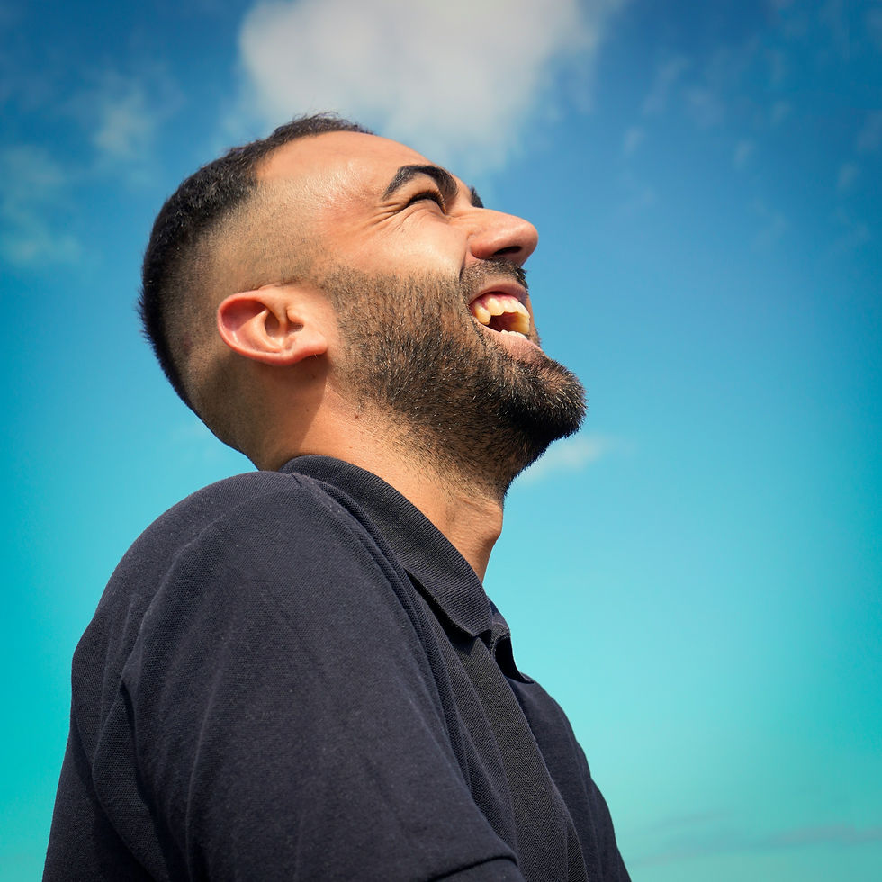 A man joyfully laughs under a clear blue sky, capturing a moment of pure happiness and freedom.