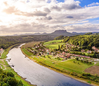 Fotograife von einem Fluss mit Ortschaft, grünen Wiesen und Bergen