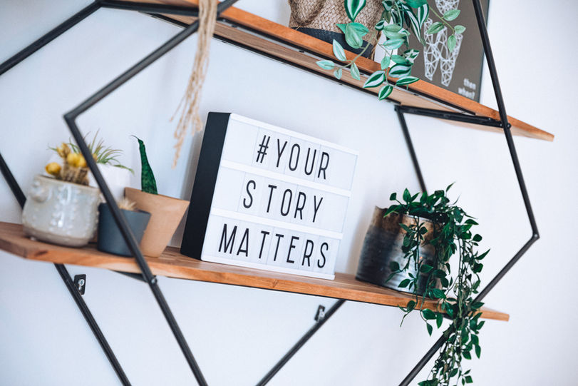 Dekoratives Wandregal in der Praxis von Christian Asperger, Spezialist für Paartherapie, Paarberatung und Eheberatung in Wien. Im Mittelpunkt steht ein Leuchtschild mit der Botschaft „#Your Story Matters“ – ein einfühlsames Statement, das den wertschätzenden und individuellen Ansatz seiner therapeutischen Arbeit unterstreicht.