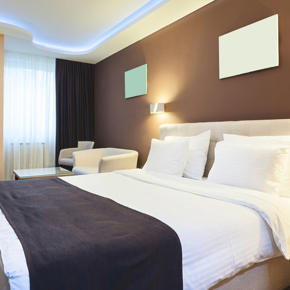 Modernes Hotelzimmer mit einem gemütlichen Doppelbett, warmen Wandfarben und eleganter indirekter Beleuchtung an der Decke. Die Wandleuchten neben dem Bett sorgen für eine angenehme Atmosphäre. Hörl Lichttechnik hat die präzise und energieeffiziente Lichtgestaltung realisiert, die den Raum harmonisch beleuchtet.