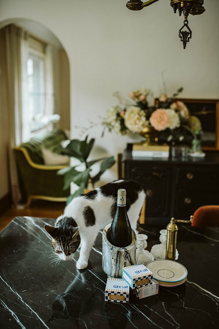 A moody, high-contrast interior shot focusing on a table setting or mantle decorated with an abundant floral arrangement, candlesticks, and books.