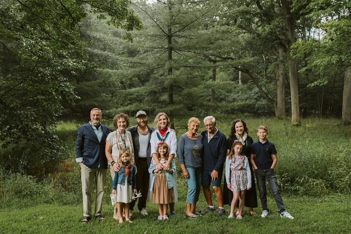 A wide, group portrait of a large extended family standing together in a grassy field backed by dense green trees.