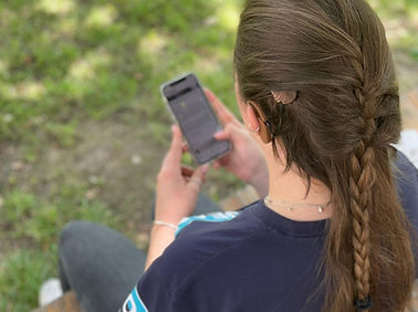 Greta Brenken ist von hinten oben zu sehen. Ihre Harre sind halb zusammengeflochten und sie schaut auf ihr Handy in der Hand.