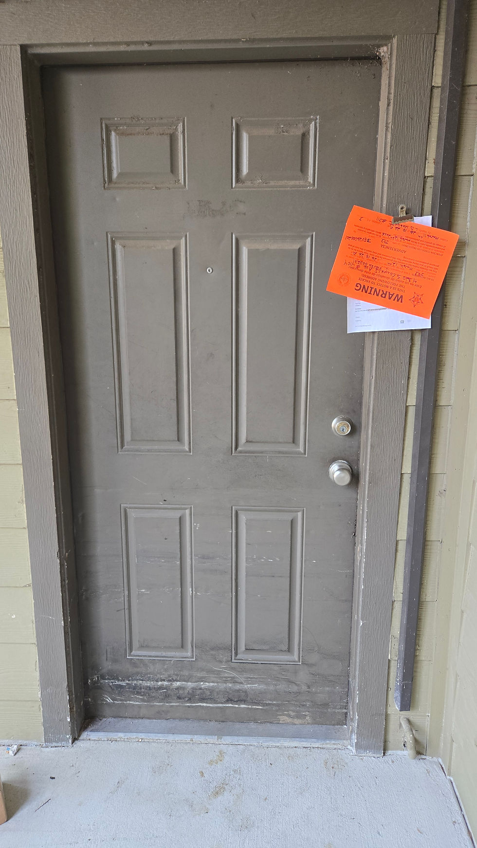 Worn wooden door with a brass knob, featuring a bright orange eviction notice with court case details, evoking a tense mood.
