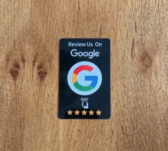 כרטיס דרג אותי עם לוגו גוגל, כוכבים וסמל NFC, מונח על שולחן עץ