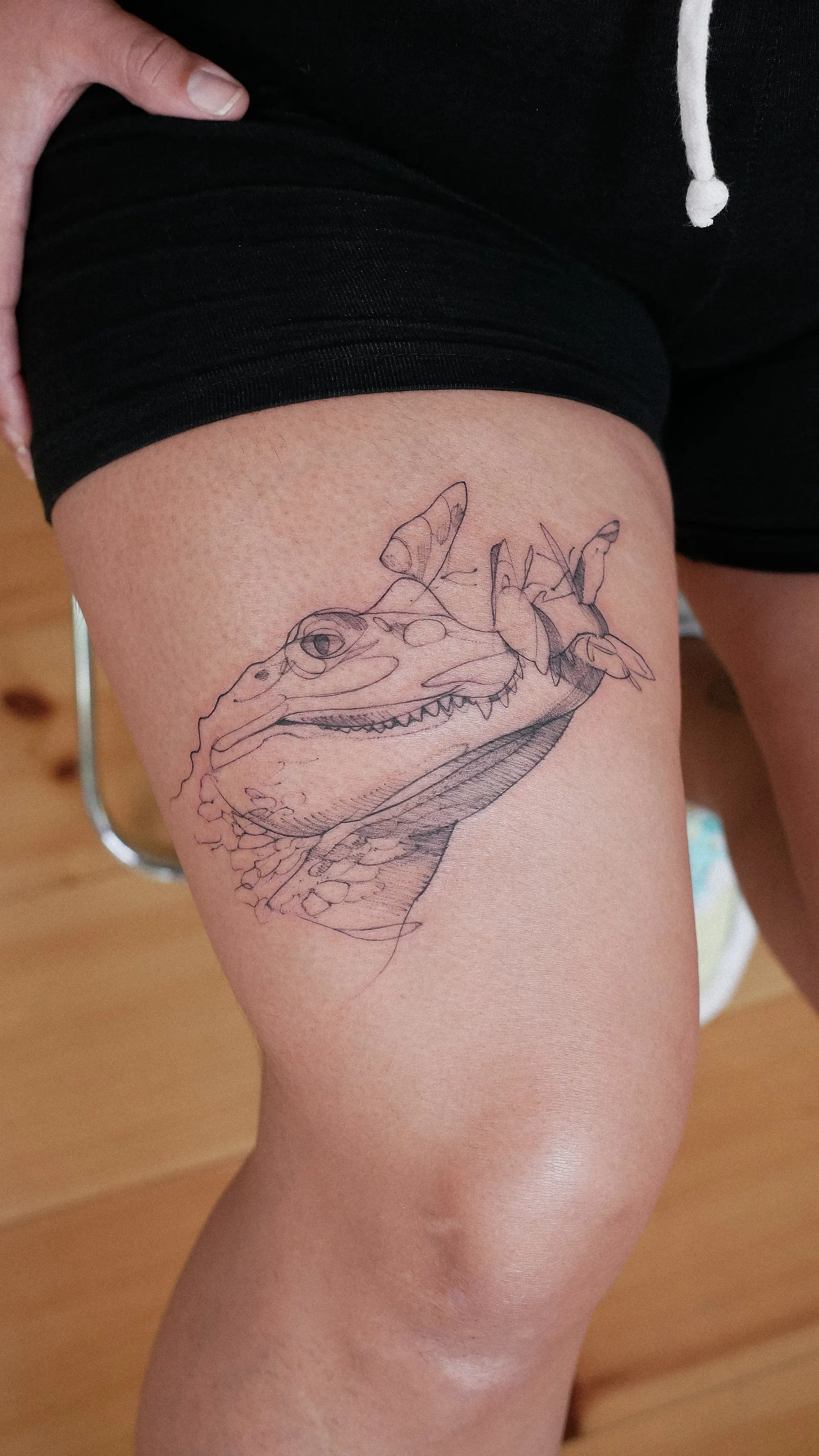Fine-Line Krokodil-Porträt-Tattoo am Oberschenkel, frisch gestochen — Schuppen und Dotwork-Schattierung in Schwarzgrau.