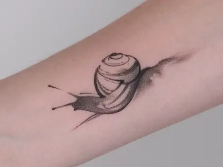 A delicate black and grey forearm tattoo depicting a small snail in motion with soft, realistic shading and fine linework accents.