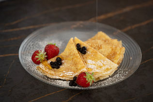 Thin French crêpes folded and dusted with sugar, served with berries on a plate
