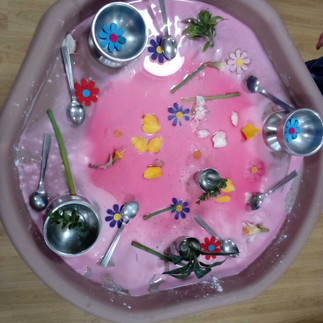 a large tray with pink oobleck and lots of strainers, flowers and spoon