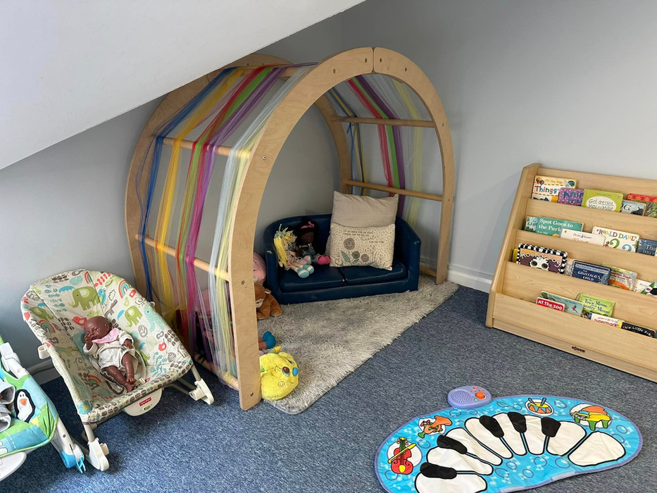 Cosy corner in baby room with soft sofa, cushions and book shelf