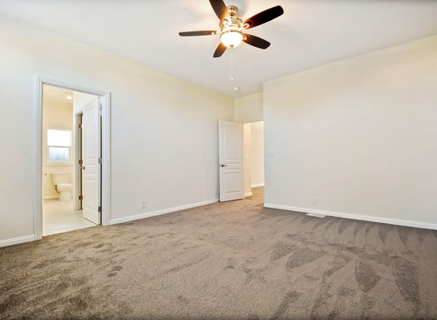 Spacious bedroom with ceiling fan, carpet, and doors to bathroom and hallway