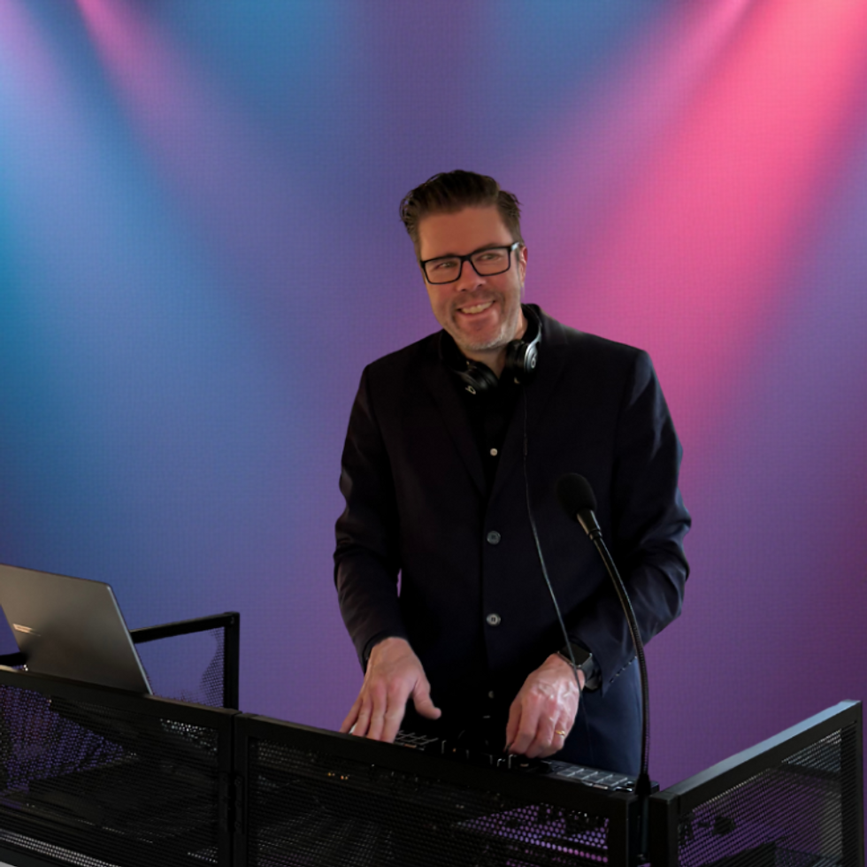 DJ Wibert ler bakom DJ-båset med blå och rosa scenbelysning